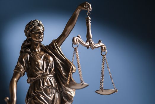 Bronze statue of Lady Justice wearing a blindfold holding up scales representing law and order over a blue background with copy space