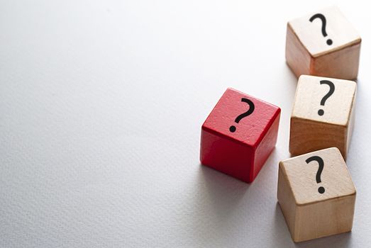 Individuality, diversity and leadership concept with three natural wood cubes and one red cube printed with question marks on a white background with copy space