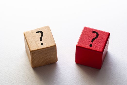 Two wooden dice or toy blocks with question marks , one natural wood and one red, on a white background in a high angle view
