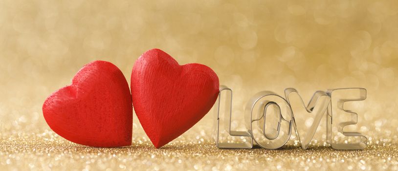 Two red handmade wooden hearts and word love on golden bright glitter lights bokeh background