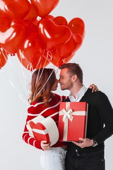 Happy smiling couple holding valentines day gifts and red balloons on white background