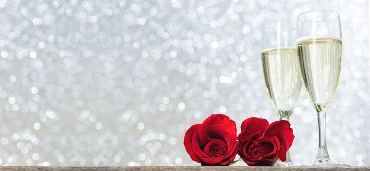 Champagne and red roses on wooden table over holiday silver glitter festive background