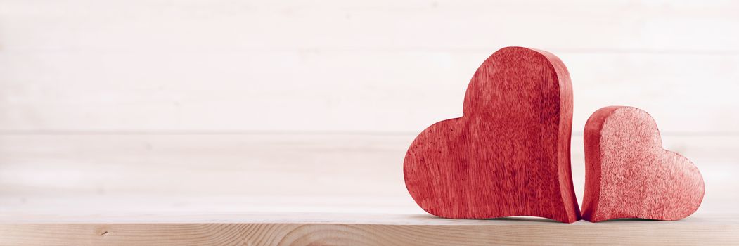 Two handmade red wooden carved hearts on light wood background couple relationship Valentine day concept