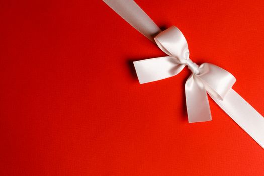 Elegant satin white ribbon bow on red background