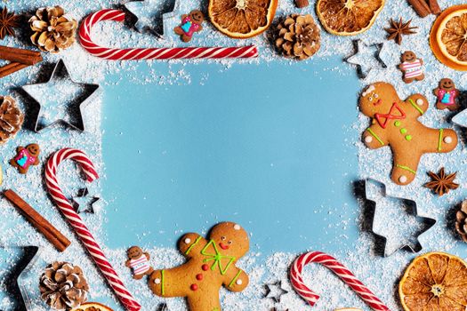 Christmas food gingerbread cookie caramel candy cane cinnamon mold shape anise orange slice on blue background with copy space