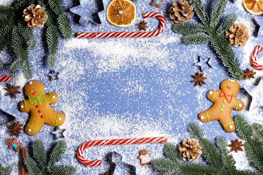 Christmas food gingerbread cookie caramel candy cane cinnamon mold shape anise orange slice and fir tree on blue background with copy space