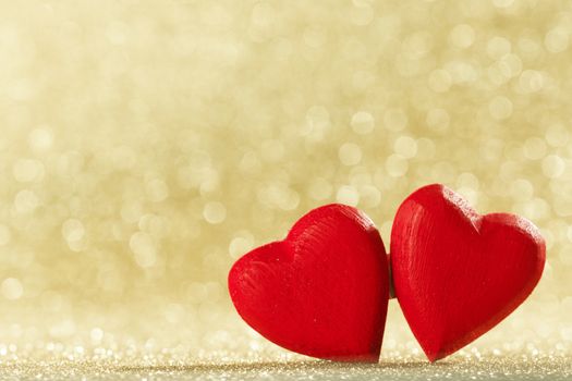 Two small handmade red wooden hearts on bright golden lights bokeh background Valentines day card