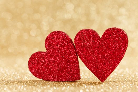 Two small handmade red glitter hearts on bright golden lights bokeh background Valentines day card