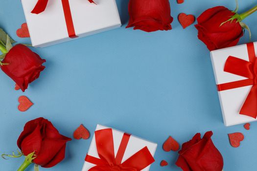 Red roses gifts and red hearts composition on blue background top view with copy space. Valentine's day, birthday, wedding, Mother's day concept. Copy space