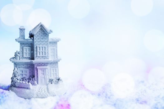 Snowy house in the snow. Winter background with colorful blue and purple shining bokeh effect. Copy space right. Shallow depth of field.