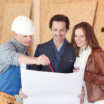 Foreman shows house design plans to smiling couple at construction site