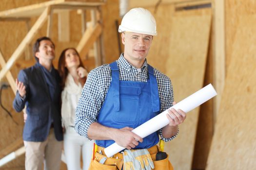 Foreman with house design plans and young excited couple at construction site