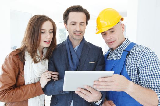 Construction worker showing blueprint plans to couple at digital tablet pc