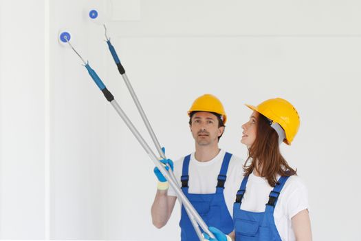 Happy young couple in uniform painting walls in their new house. Repair, construction and mortgage concept.