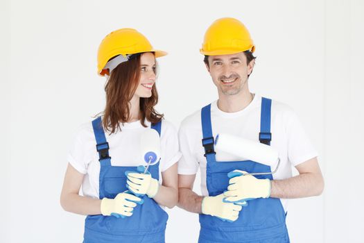 Two happy house painters in uniform holding paint rollers in new house. Repair, construction and mortgage concept.