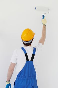 Male worker in uniform painting walls in new house. Repair, construction and mortgage concept.