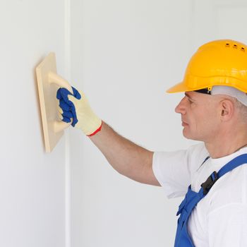 Male worker finishing works aligning the wall after puttying