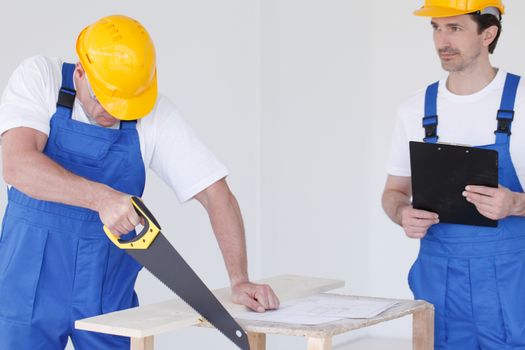 Two workmen in protective workwear with saw and folder at construction site