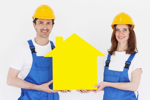 Two happy smiling workers hold yellow house model outdoors at construction site