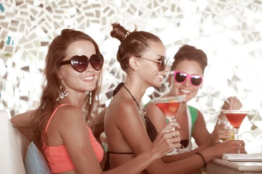 Three female friends sitting in summer cafe drinking cocktails