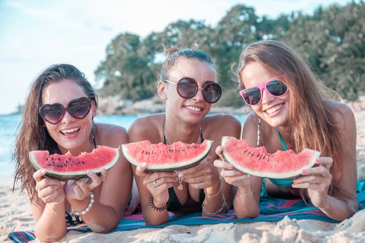 Happy smiling female friends eating watermelon on beach