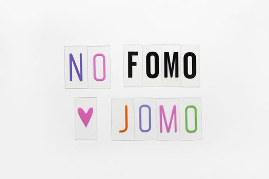 Abbreviation words FOMO, JOMO on transparent plastic on white background. FOMO means Fear Of Missing Out. JOMO - Joy Of Missing Out. Opposition, choice, social problem, digital detox. Flat lay.