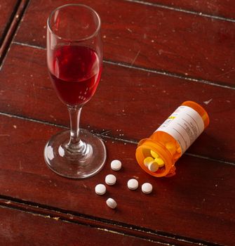 glass of red wine next to a bottle of spilled pills