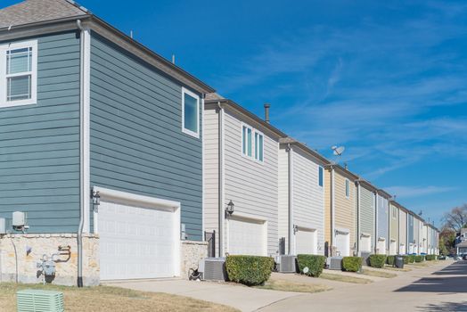 Corner house and back alley of new development residential community, line of two-car garage door in Coppell, Texas. Colorful two story houses row well trim landscape near Dallas, outdoor AC units