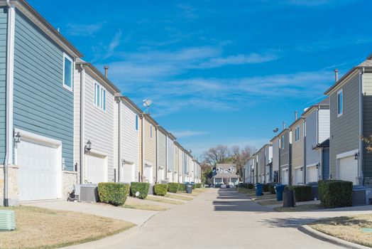 Back alley of residential community, small concrete pathway leading to country-style house. Line of two-car garage door in Coppell, Texas. Colorful two story houses row well trim landscape near Dallas