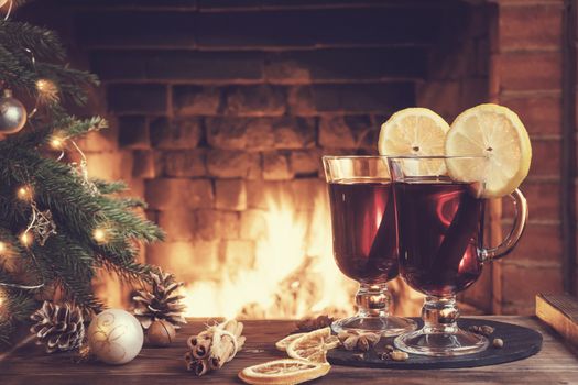 Christmas composition - two glasses with mulled wine on a wooden table near a Christmas tree opposite a burning fireplace.