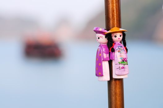 Selective focus couple handicraft magnetic wooden puppets in Vietnamese traditional costumes. Natural set with boat and ocean background