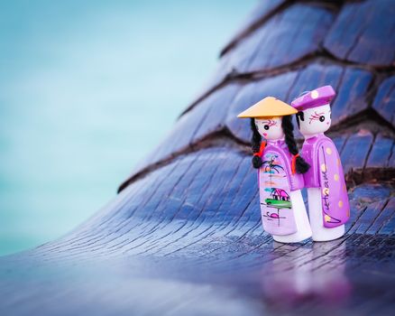Close-up a couple handicraft magnetic wooden puppets in Vietnamese traditional costumes. Famous Vietnamese dolls souvenirs in natural set with boat and ocean background. Selective focus