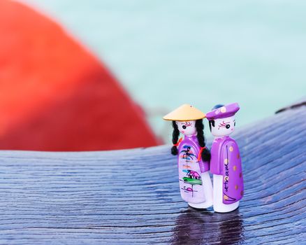 Close-up a couple handicraft magnetic wooden puppets in Vietnamese traditional costumes. Famous Vietnamese dolls souvenirs in natural set with boat and ocean background. Selective focus