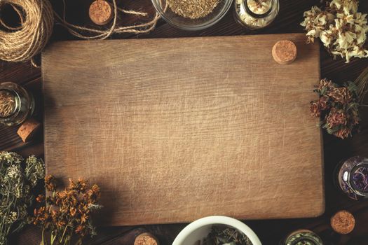 Cutting wooden board with various dried medicinal herbs and devices. Homeopathy and herbal treatment concept, place for text, copy space, top view, flat lay.