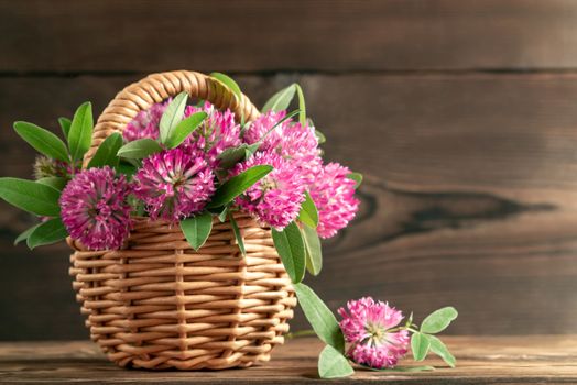 Bouquet of pink clover in a wicker basket on a wooden table on a summer morning.