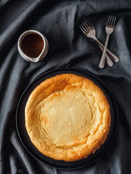 Plate with whole cheesecake pie on table with tablecloth. Classic cheesecake, caramel and dessert forks. Vertical. Top view or flat lay.