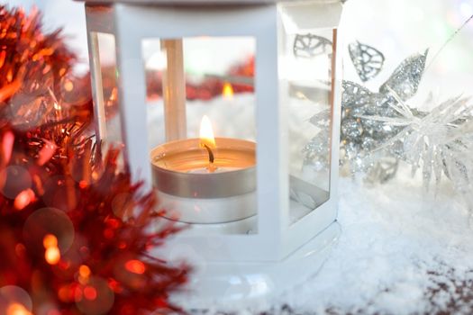 Festive background with red, glittery silver christmas decoration. White lantern on the snow with candlelight. Shallow depth of field. Defocused light, bokeh effect.