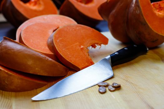 The food on thanksgiving. A bright orange pumpkin is cut into pieces with a kitchen knife and lies on a wooden Board.