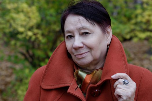 Portrait of an old woman in a bright terracotta coat in an autumn Park