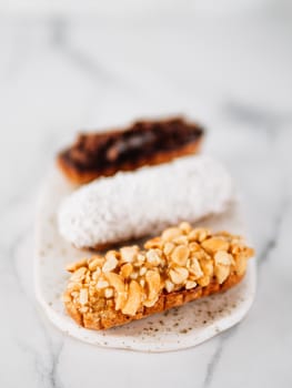 Set of three homemade eclairs on marble background. Close up view of delicious healthy profitroles with different decor elements - chocolate, peanut and sherdded coconut. Vertical.