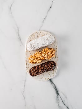 Set of three homemade eclairs on marble background. Top view of delicious healthy profitroles with different decor elements - chocolate, peanut and sherdded coconut. Vertical