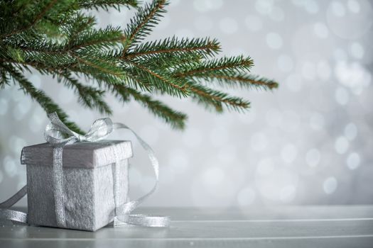 Silver Christmas new year gift with curly streamer ribbon bow over glittering bokeh lights background under fir tree