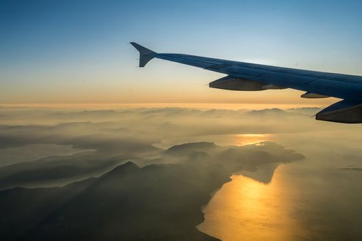 View on passenger aircraft left wing. Sun shines as a light beam over the wing. Thick clouds below airplane are illuminated by the. Golden sun. Horizontal view