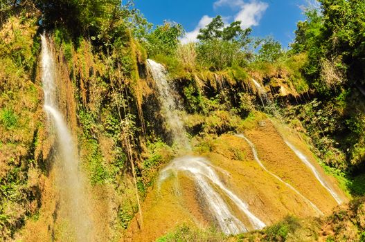 Spectacular view of fall gushes down its slope, white curtain flowing in Dai Yem (Pink Blouse) waterfall, Moc Chau District, Son La Province. Cool refreshing spring pouring on limestone wall, blue cloud sky