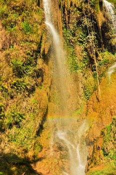 Rainbow over small white current at Dai Yem (Pink Blouse) waterfall in Muong Sang Commune, Moc Chau, Son La, Vietnam. Fall gushes down its slope with small and medium rocks in various shapes