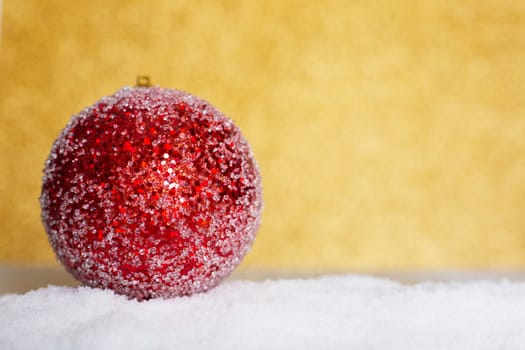 Christmas red ball on snow over golden glitter background with copy space for text