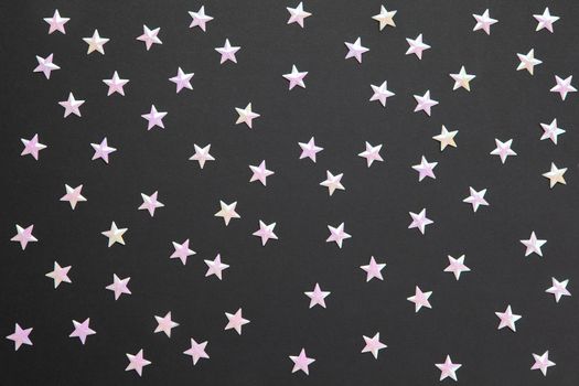 Chaotic pattern from numerous pearl confetti in form of small stars on black paper background. Celebration, holidays, sales, fashion concept. Horizontal. Flatlay. Blank for greeting cards.