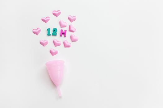 Pink menstrual cup on white background with hearts and designation of use time, 12 hours, laid out in colored numbers and letter. Concept zero waste, savings. Flat lay, copy space. Horizontal.