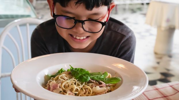 Boy happy eating spaghetti carbonara recipe - people enjoy with famous Italian dish food concept