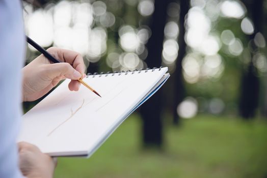 Relax woman painting water colour art work in green garden forest nature - people with creative art in nature stress reduction and meditation concept